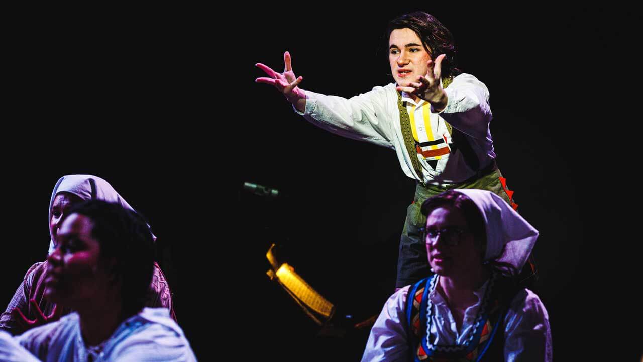 A male student actor on stage in a spotlight