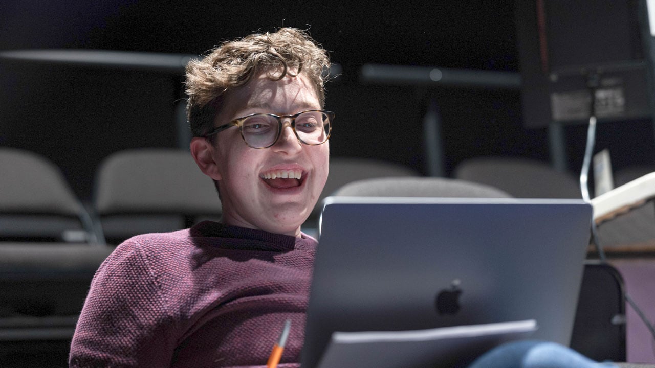 A theater student smiling on their computer in the new play lab