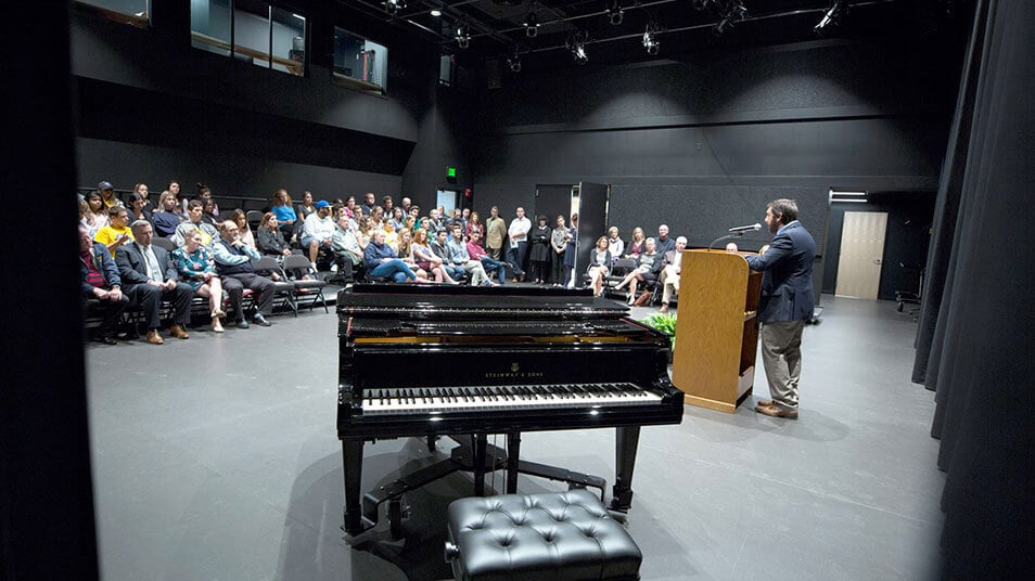 Theater director Kevin Daly gives opening remarks at a podium onstage to a large crowd